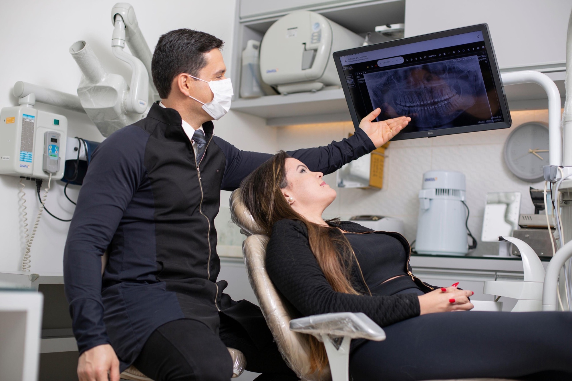 Dr. Lúcio Veiga analisando radiografia panorâmica com uma paciente na clínica